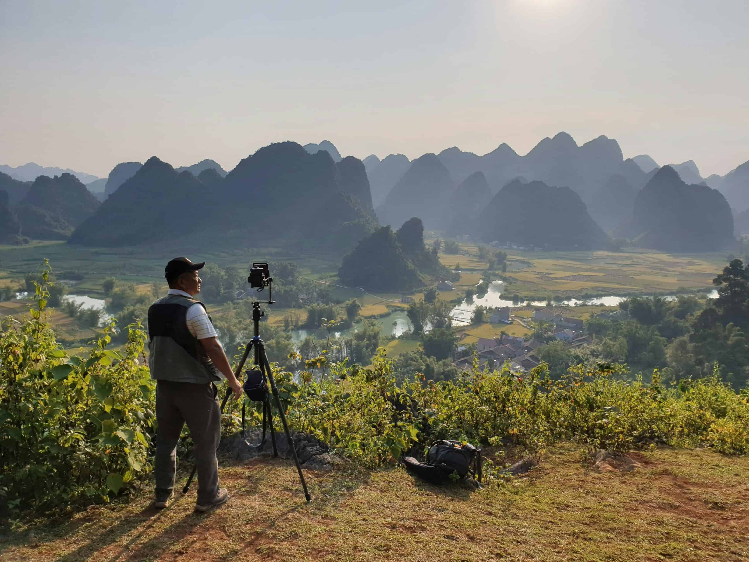 Man standing near tripod with mountains in the background